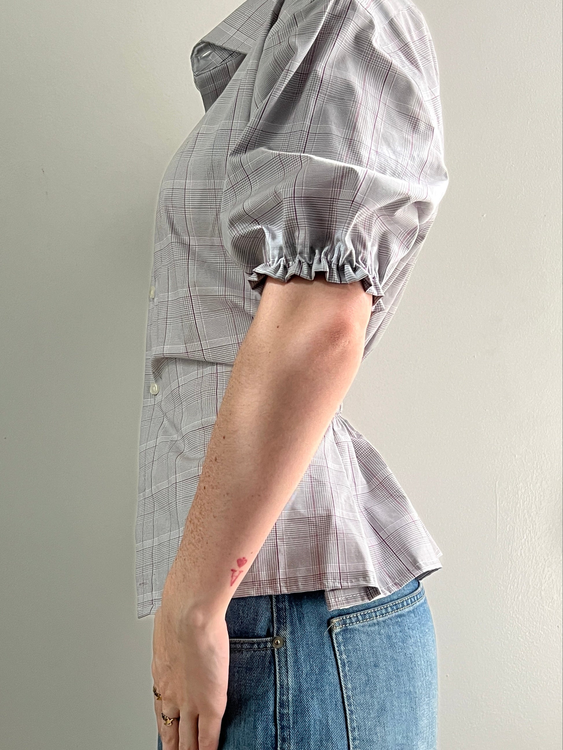 Female wearing a plaid short sleeve puff sleeve button down blouse with a cinched back facing left.