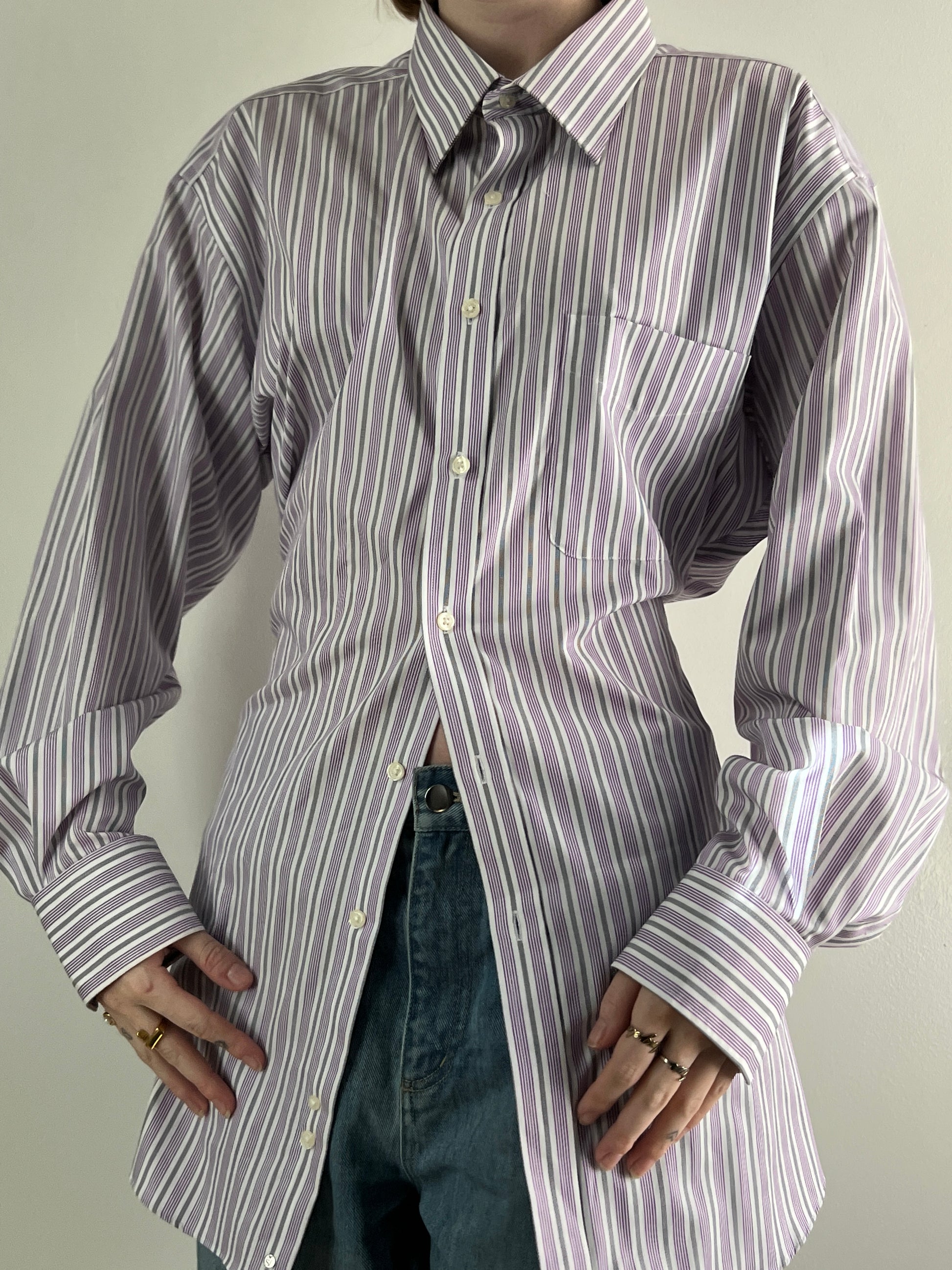 Female wearing a purple and gray striped blouse with a cinched back facing front.