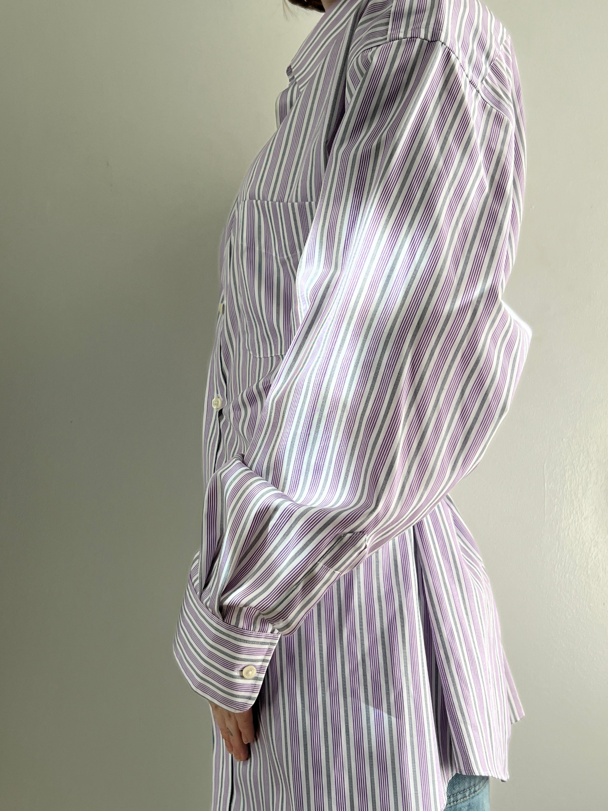 Female wearing a purple and gray striped blouse with a cinched back facing left.