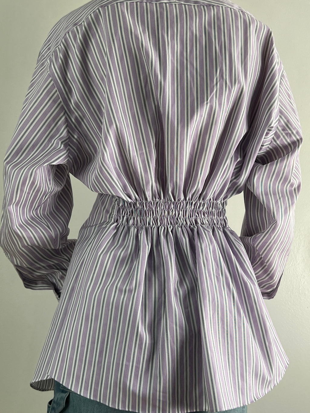 Female wearing a purple and gray striped blouse with a cinched back.