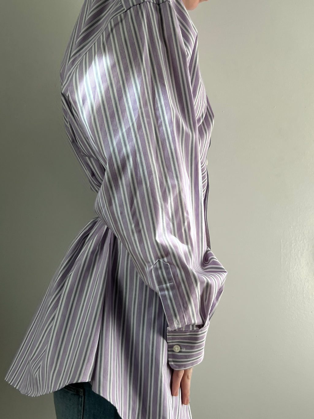 Female wearing a purple and gray striped blouse with a cinched back facing right.