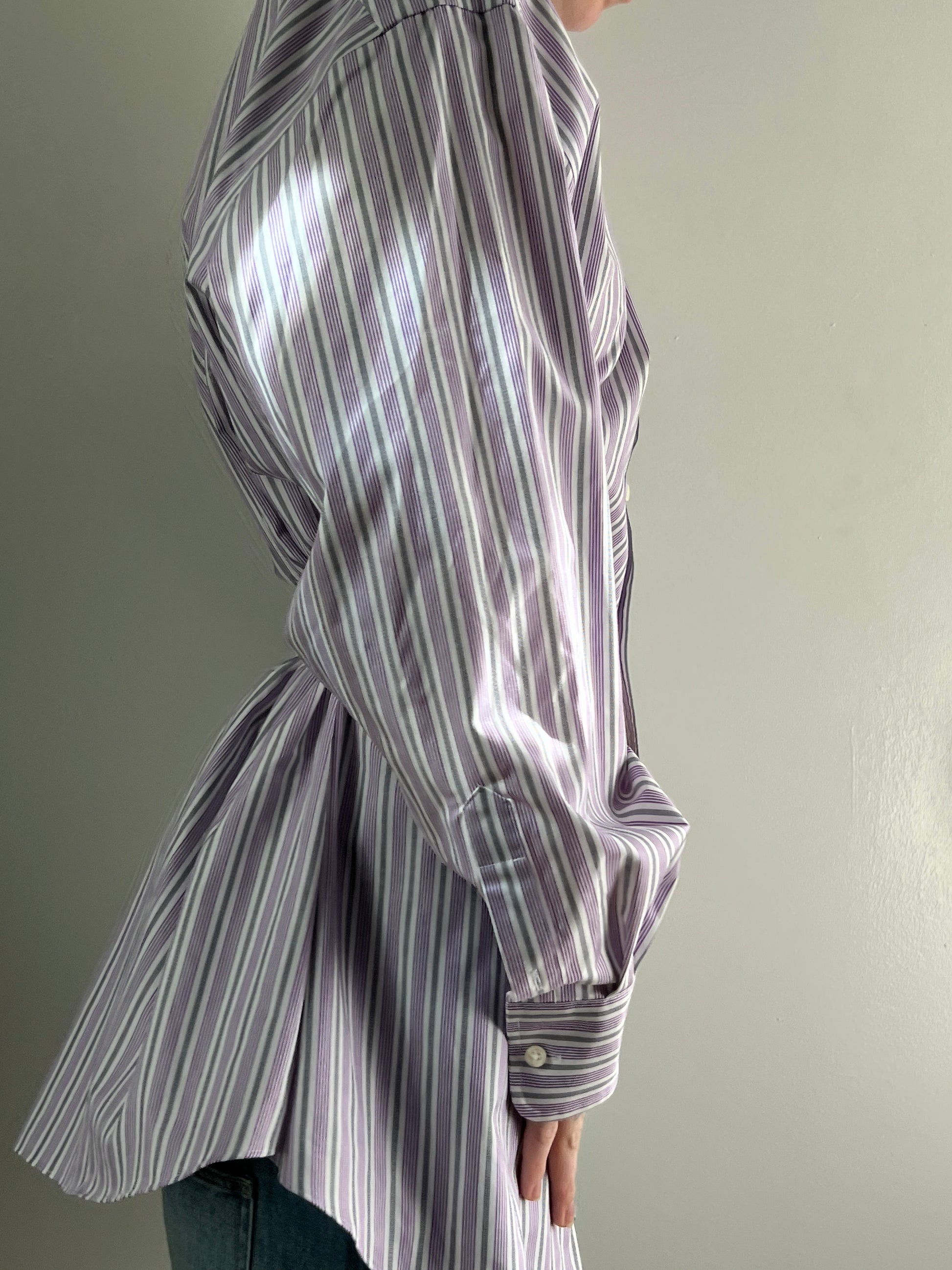 Female wearing a purple and gray striped blouse with a cinched back facing right.