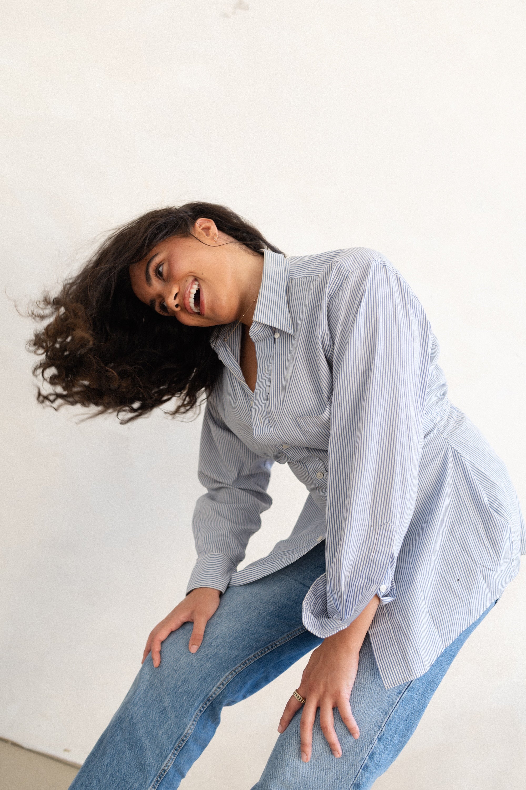 Woman wearing a light blue striped shirt and jeans against a white background