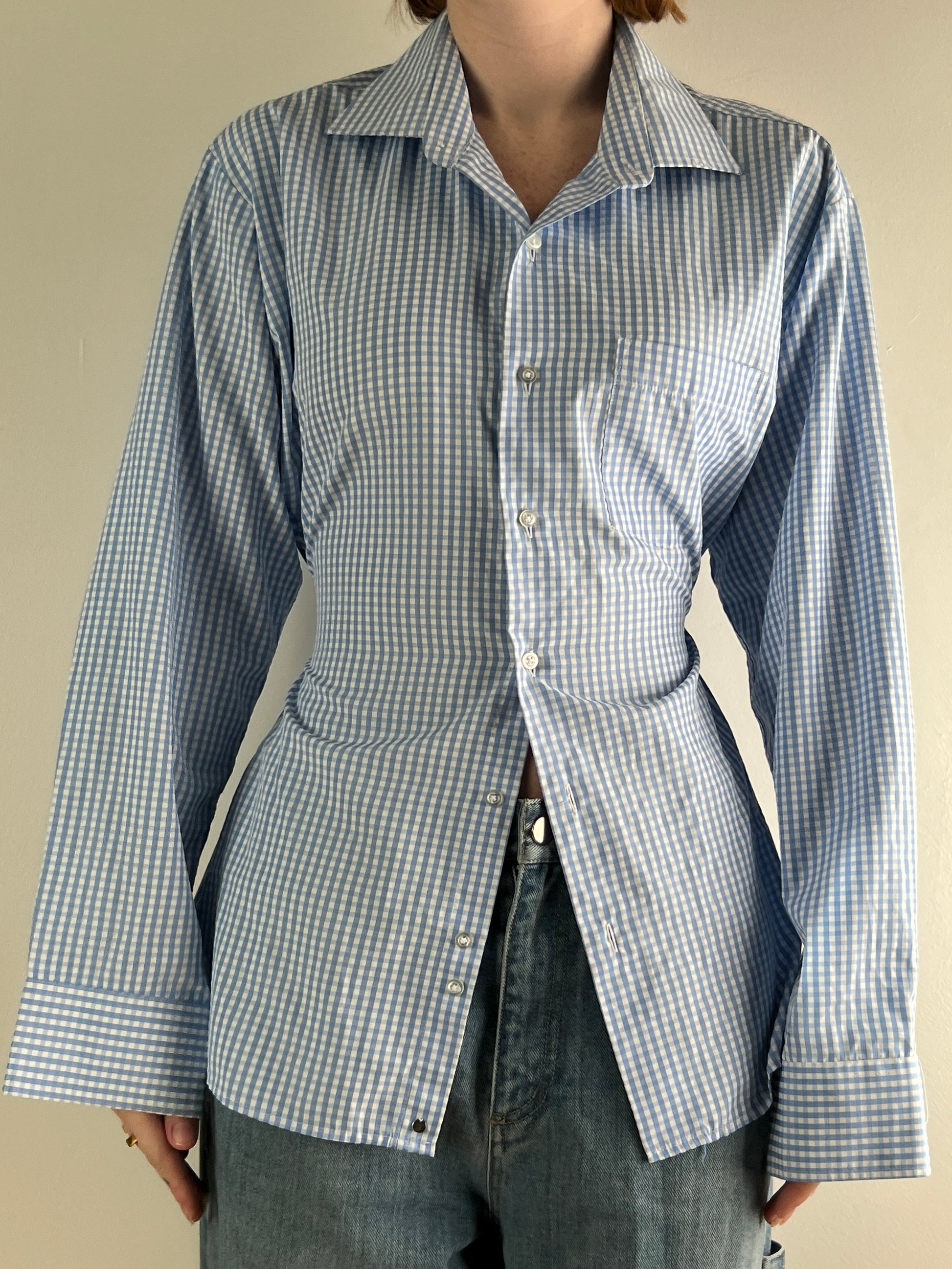 Female wearing a baby blue gingham button down blouse with a cinched elastic back facing front.