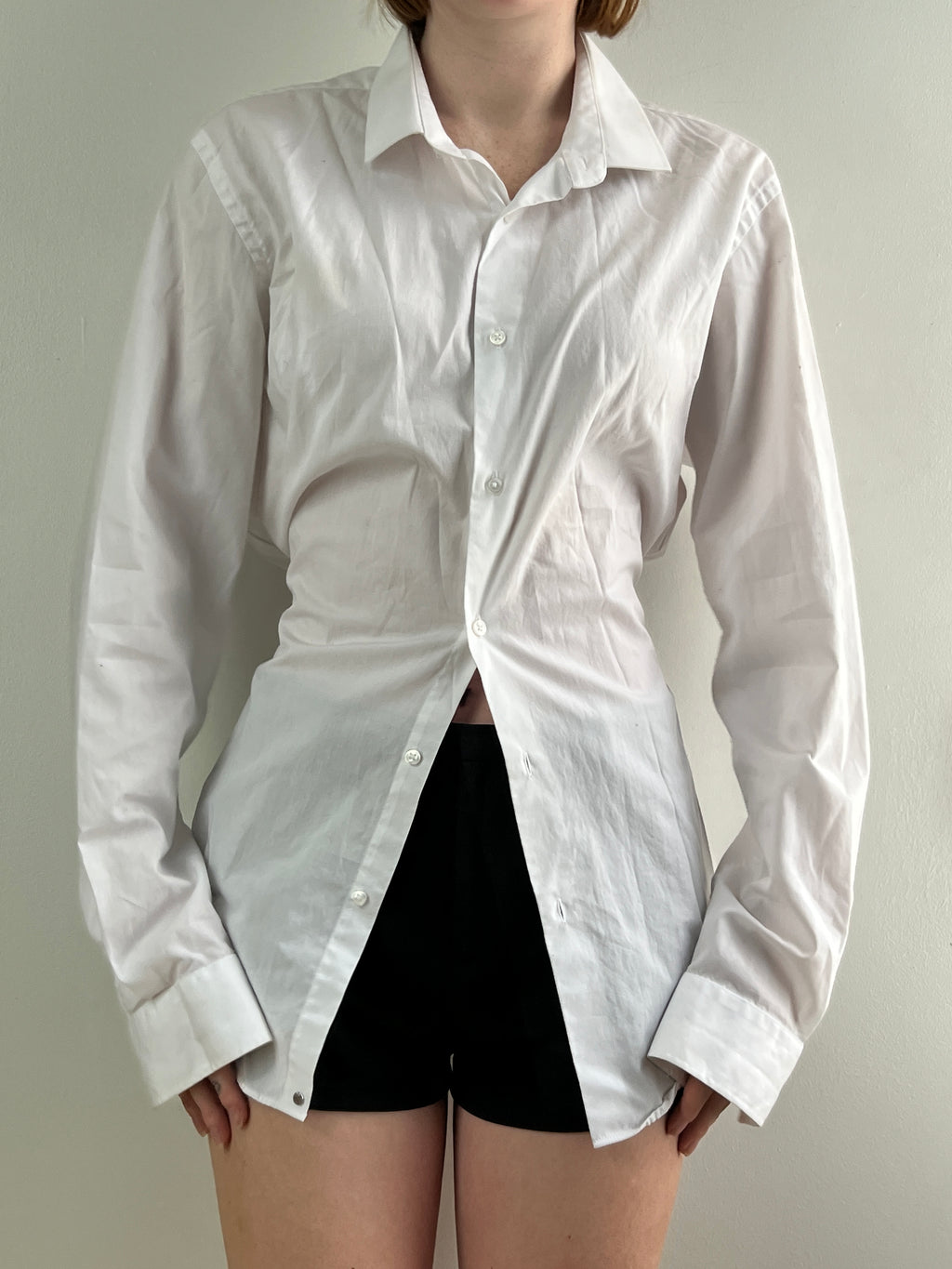 Female wearing a white button down blouse with a cinched back facing front.