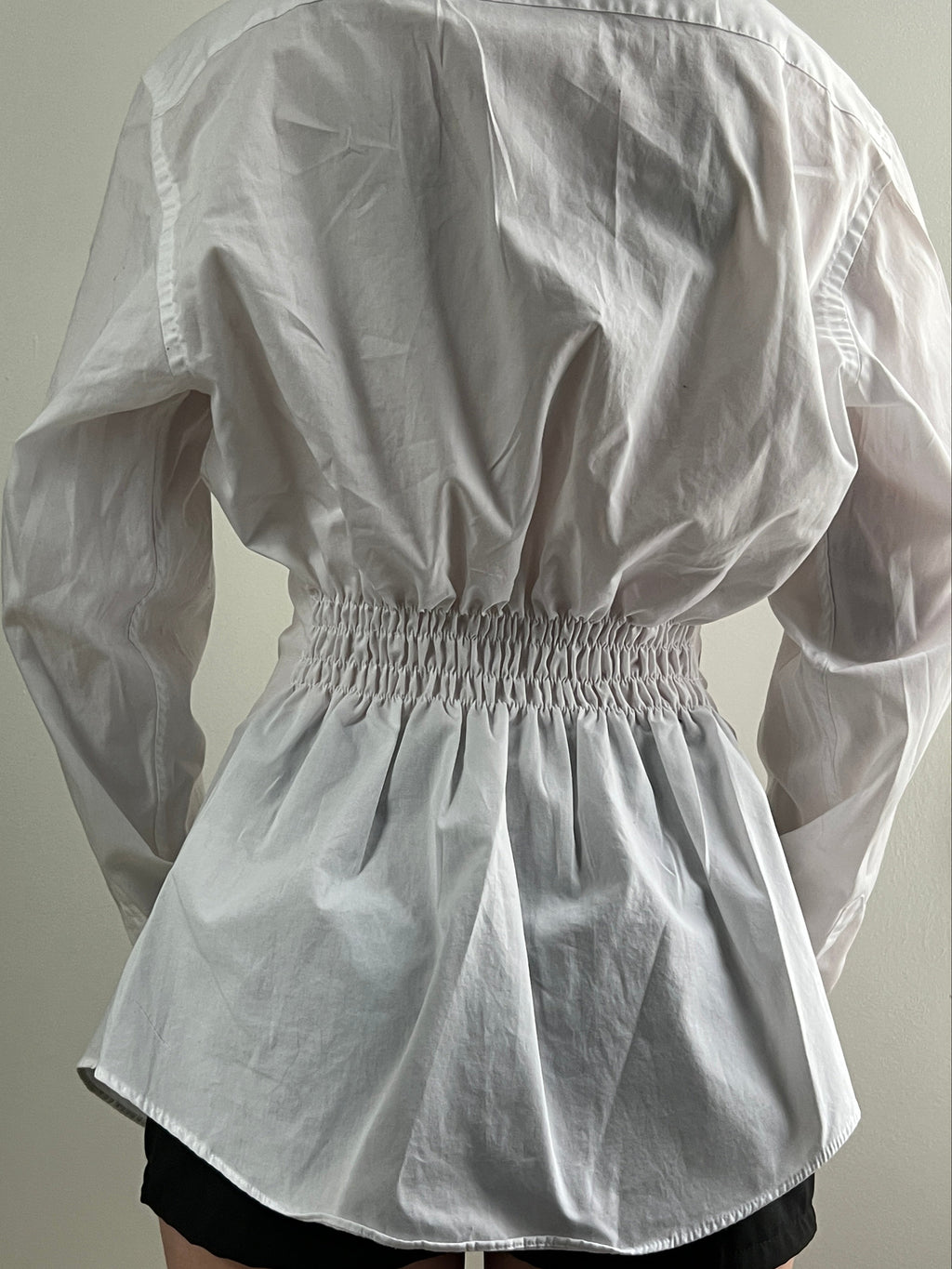 Female wearing a white button down blouse with a cinched back.